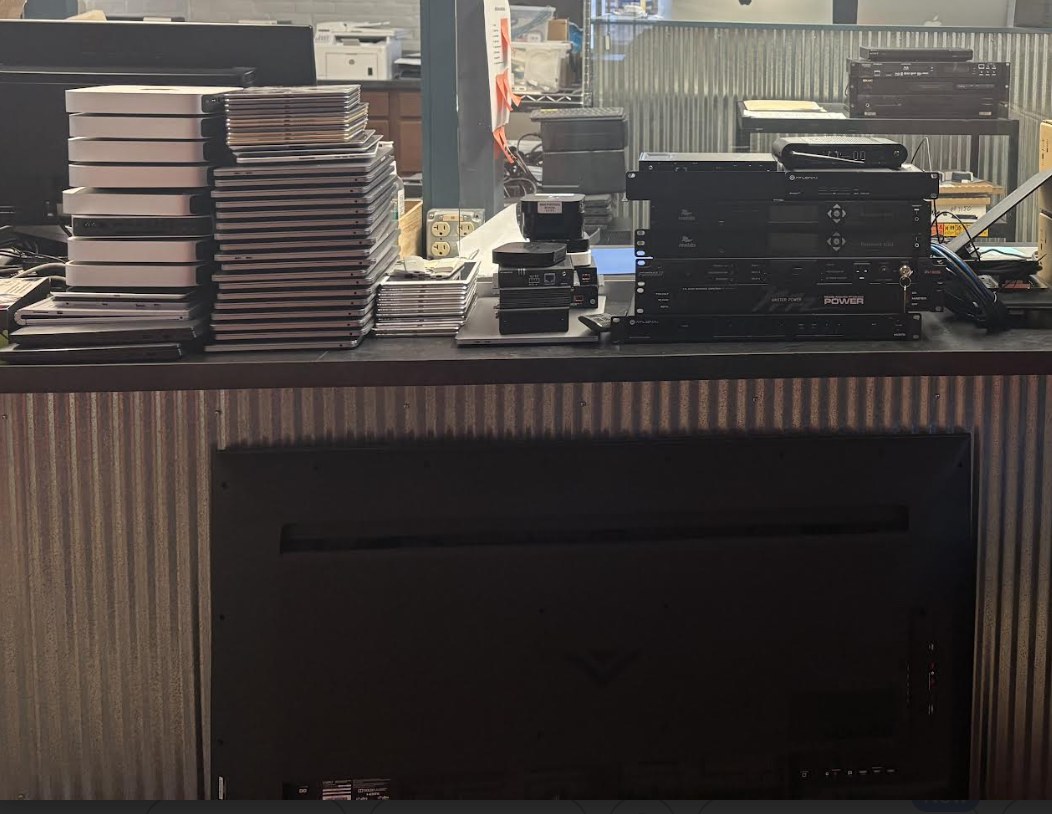 Stacked MacBooks, AV gear, monitors, and network equipment from a school refresh